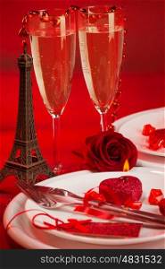 Image of red luxury table setting, white festive plate and two glass of champagne decorated with small Eiffel tower and fresh rose flower, dinner in Paris, honeymoon in France, Valentine day&#xA;