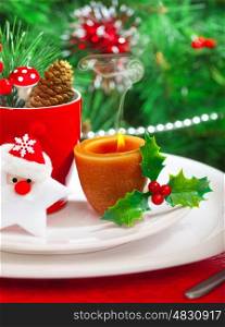 Image of romantic Christmastime dinner with warm candle light, red coffee cup decorated with Santa Claus star and fir cone, beautiful white dinnerware on Christmas tree background, New Year party&#xA;