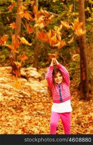 Image of small cute female child enjoying autumn nature, little pretty girl playing game in fall park, adorable sweet kid throwing up old dry foliage, carefree baby, happy childhood