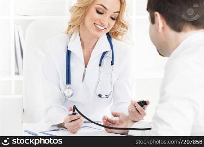 Image of smiling female doctor measuring blood pressure of patient on tonometer. Doctor measuring blood pressure