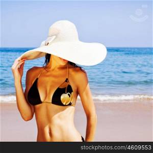 Image of stylish girl on the beach, beautiful woman with perfect body standing on coastline, attractive female enjoying sunny summer day, sexy model wearing great fashionable hat on sea coast&#xA;&#xA;