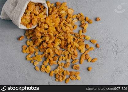 Image of sweet dried grapes spread from rustic sack, isolated over grey background. Yellow raisins containing useful vitamins