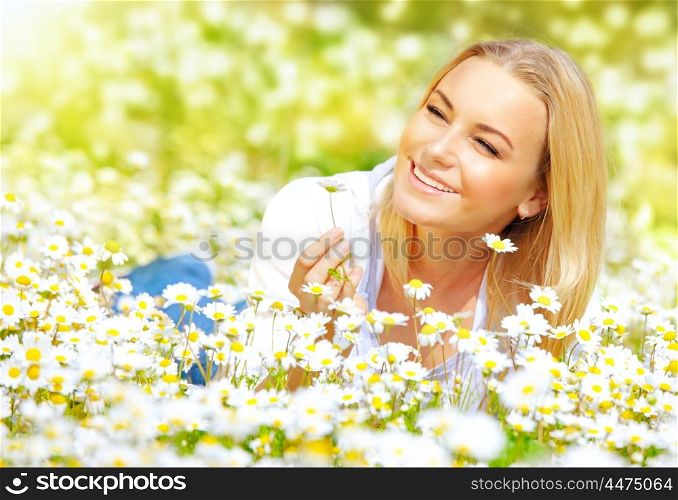 Image of sweet girl lying down on daisy glade and enjoying warm sun light, beautiful woman holding in hand little camomile flower, recreation on floral field, relaxation in rural place, spring holiday