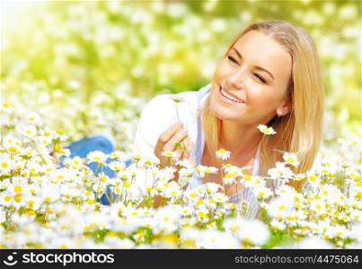 Image of sweet girl lying down on daisy glade and enjoying warm sun light, beautiful woman holding in hand little camomile flower, recreation on floral field, relaxation in rural place, spring holiday