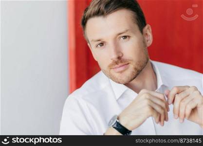 Image of thoughtful self confident male entrepreneur in white shirt, listens attentively his business partner during meeting, poses against white and red background. People, career and lifesyle