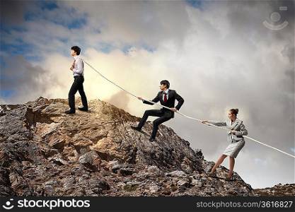 Image of three businesspeople pulling rope atop of mountain