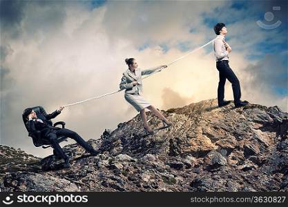 Image of three businesspeople pulling rope atop of mountain