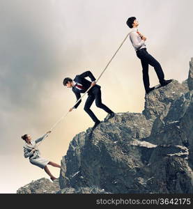 Image of three businesspeople pulling rope atop of mountain