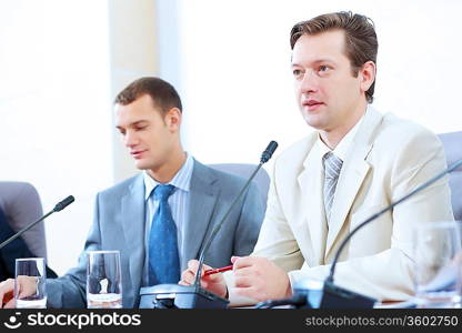 Image of two businesspeople sitting at table at conference speaking in microphone