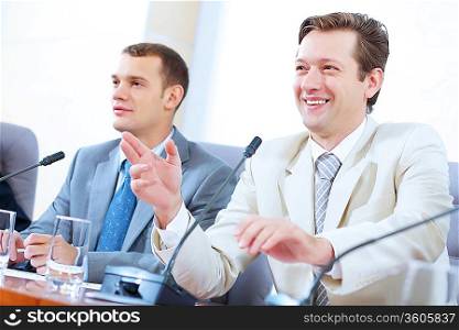 Image of two businesspeople sitting at table at conference speaking in microphone
