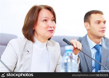 Image of two businesspeople sitting at table at conference speaking in microphone