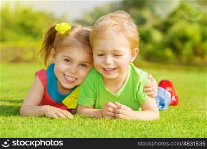 Image of two happy children having fun in the park, brother and sister lying down on green grass, best friends playing outdoors in spring, adorable little girl with cute boy enjoying springtime nature