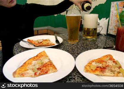 image of woman&#39; s hand pouring beer in a glass and pizza