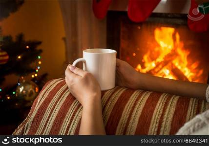 Image of woman sitting on sofa by the fireplace and holding cup of tea