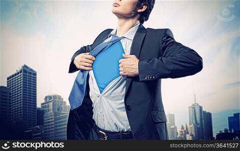 Image of young businessman showing superhero suit underneath his shirt standing against city background