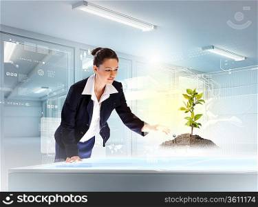 Image of young businesswoman touching sprout on high-tech picture