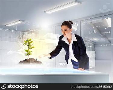 Image of young businesswoman touching sprout on high-tech picture