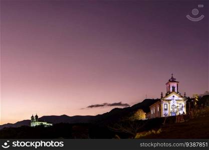 Image with baroque style illuminated churches on top of the hill in Ouro Preto, Minas Gerais illuminated during sunset. Image with baroque style illuminated churches on top of the hill