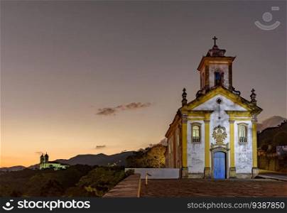 Image with illuminated baroque style churches on top of the hill in Ouro Preto, Minas Gerais illuminated during dusk. Image with illuminated baroque style churches