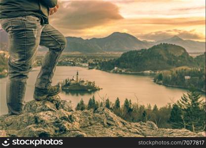 Image with the legs of a tourist man climbed on rocks above the lake Bled in Slovenia, looking at the beautiful sunrise and the Julian Alps