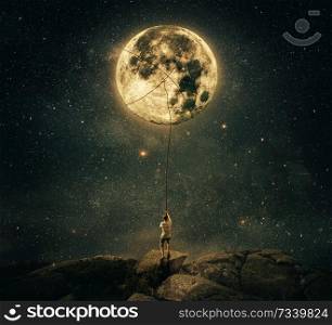 Imaginary view as a young man, holding a rope, try to catch and pull the full moon from the night sky. Achievement and hard determination concept.