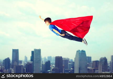 imagination, freedom, childhood, movement and people concept - boy in red superhero cape and mask flying in air over city background. boy in red superhero cape and mask flying on air