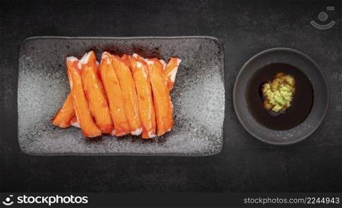 imitation Alaska crab sticks with Wasabi and Shoyu soy sauce in ceramic plate on dark tone texture background, top view