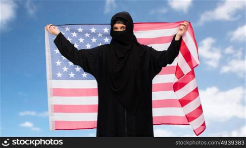 immigration and people concept - muslim woman in hijab with american flag over blue sky and clouds background. muslim woman in hijab with american flag