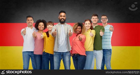immigration, diversity, race, ethnicity and people concept - international group of happy smiling men and women showing thumbs up over german flag background. international group of people showing thumbs up