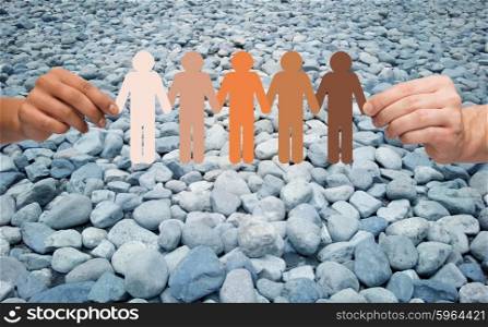 immigration, unity, population, race and humanity concept - multiracial couple hands holding chain of paper people pictogram over stones in desert background