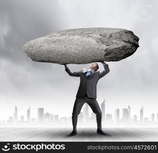 Impending problems. Powerful businessman holding huge stone above head