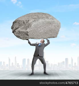 Impending problems. Powerful businessman holding huge stone above head