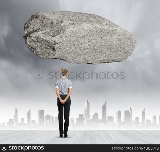 Impending problems. Rear view of businesswoman looking at urban scene with huge stone above