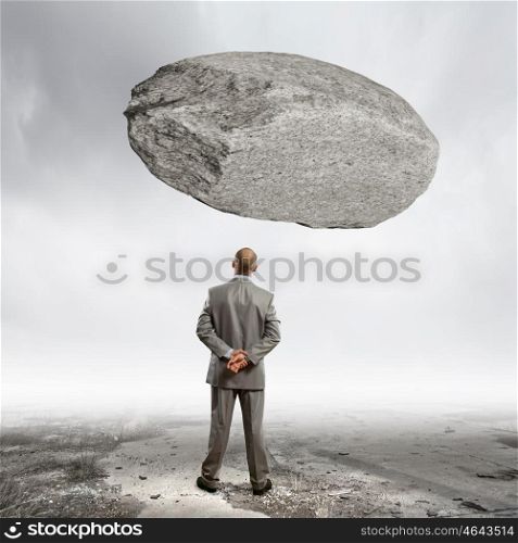 Impending problems. Rear view of confident businessman with huge stone above