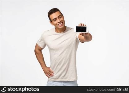 Impressed, satisfied good-looking hispanic guy in good shape, promote fitness application, looking mobile screen with pleased smile, stretch hand, holding smartphone, advertise app, white background.. Impressed, satisfied good-looking hispanic guy in good shape, promote fitness application, looking mobile screen with pleased smile, stretch hand, holding smartphone, advertise app, white background