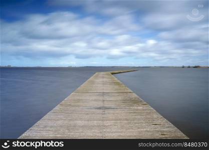 Impressive clouds skies and a calm deserted lake scene in The netherlands at a landing spot for boats before the start of the tourist season.. Wooden jetty at the lake with exaggerating cumulus clouds