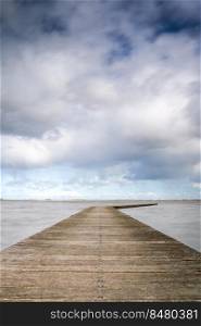 Impressive clouds skies and a calm deserted lake scene in The netherlands at a landing spot for boats before the start of the tourist season.. Long Wooden construction jetty at the lake with Dutch cloudy skies