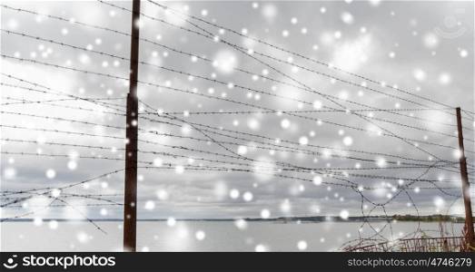 imprisonment and restriction concept - broken barb wire fence over gray sky and sea shore with snow. broken barb wire fence over gray sky and sea