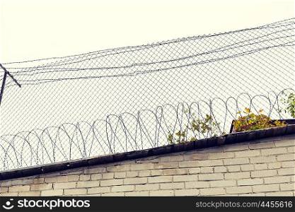 imprisonment, restriction concept - barb wire fence and brick wall over gray sky