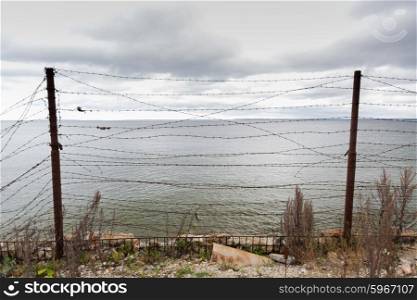 imprisonment, restriction concept - barb wire fence over gray sky and sea