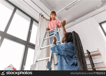 improvement and renovation concept - happy smiling women with ladder hanging curtains at home and making high five gesture. women hanging curtain at home and making high five