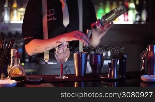 in a nightclub or pub, a professional bartender preparing a cocktail with ice a mix of alcohol. The barman measure quantities for a perfect cocktail. concept: disco, fun, friends, cocktail.