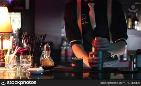 in a nightclub or pub, a professional bartender preparing a cocktail with ice a mix of alcohol. The barman measure quantities for a perfect cocktail. concept: disco, fun, friends, cocktail.