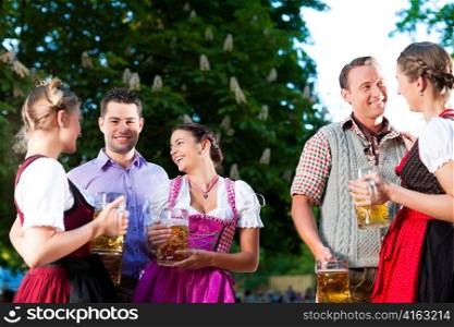 In Beer garden - friends in Tracht, Dirndl and Lederhosen drinking a fresh beer and talk in Bavaria, Germany