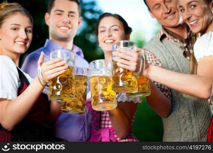In Beer garden - friends in Tracht, Dirndl and Lederhosen drinking a fresh beer in Bavaria, Germany