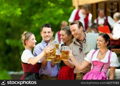 In Beer garden in Bavaria, Germany - friends in Tracht, Dirndl and Lederhosen and Dirndl standing in front of band