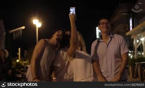 In evening in city of Perea, Greece young company of 3 men and 1 girl in street taking selfies on a mobile phone