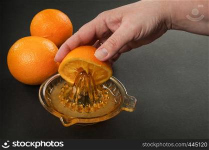 in hand manual juicer with oranges on dark background