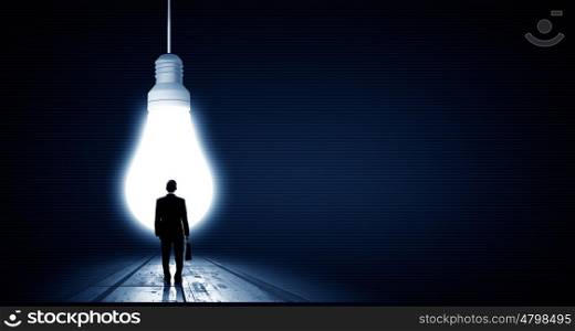 In light of idea. Rear view of businessman with suitcase looking at light bulb