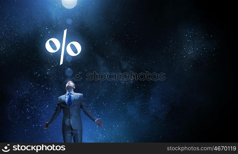 In light of success. Businessman with hands spread apart standing in light and percent sign above